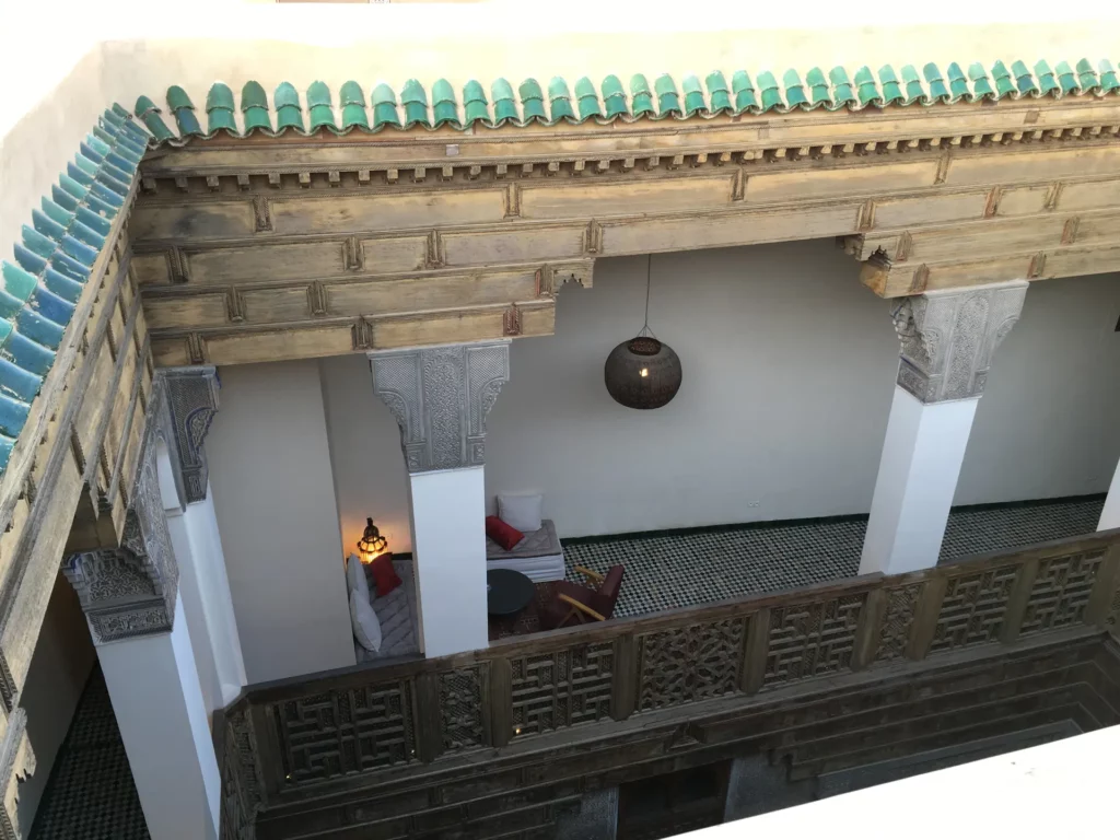 intérieur d’un riad traditionnel à Marrakech avec galerie à colonnes, boiseries sculptées et décoration marocaine autour du patio