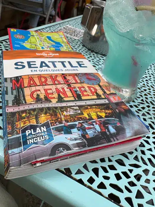 Un guide touristique destiné aux visiteurs de Seattle, posé sur une table métallique bleue à côté d'un verre de boisson glacée bleue.